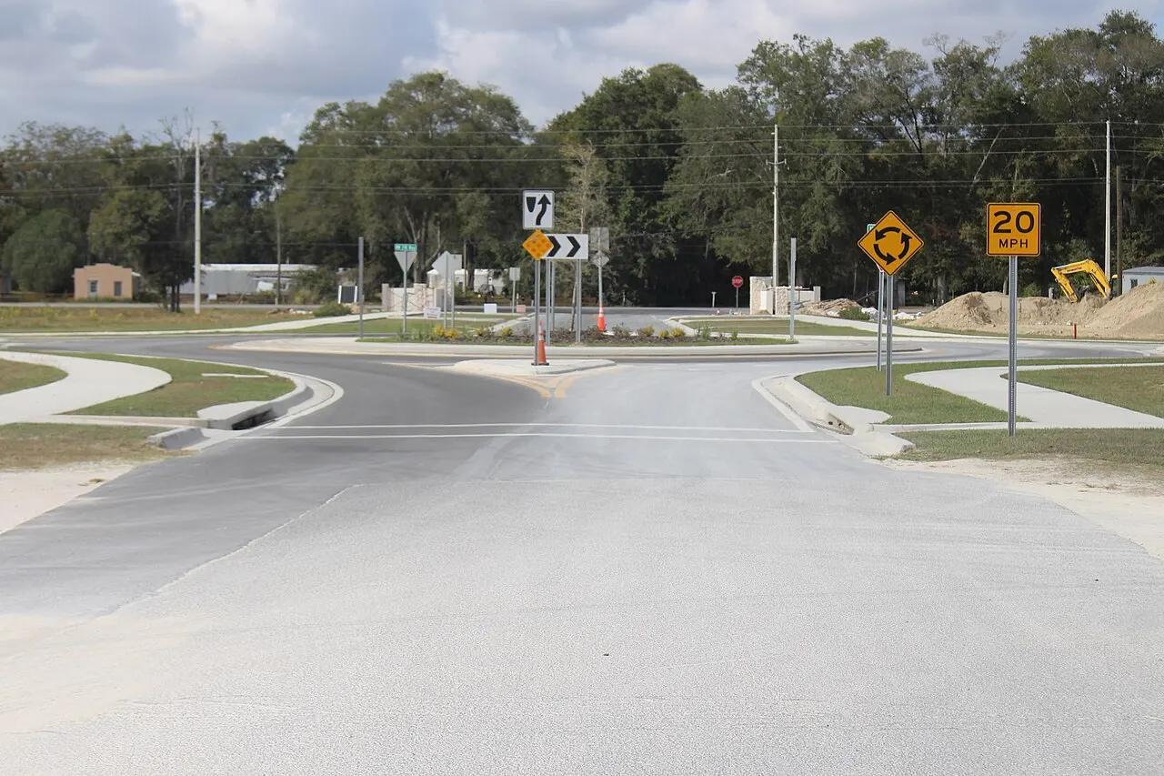 The westbound approach to a roundabout on NW 16th Avenue in Newberry, Florida, with a roundabout warning sign and a 20 mph sign beside the road