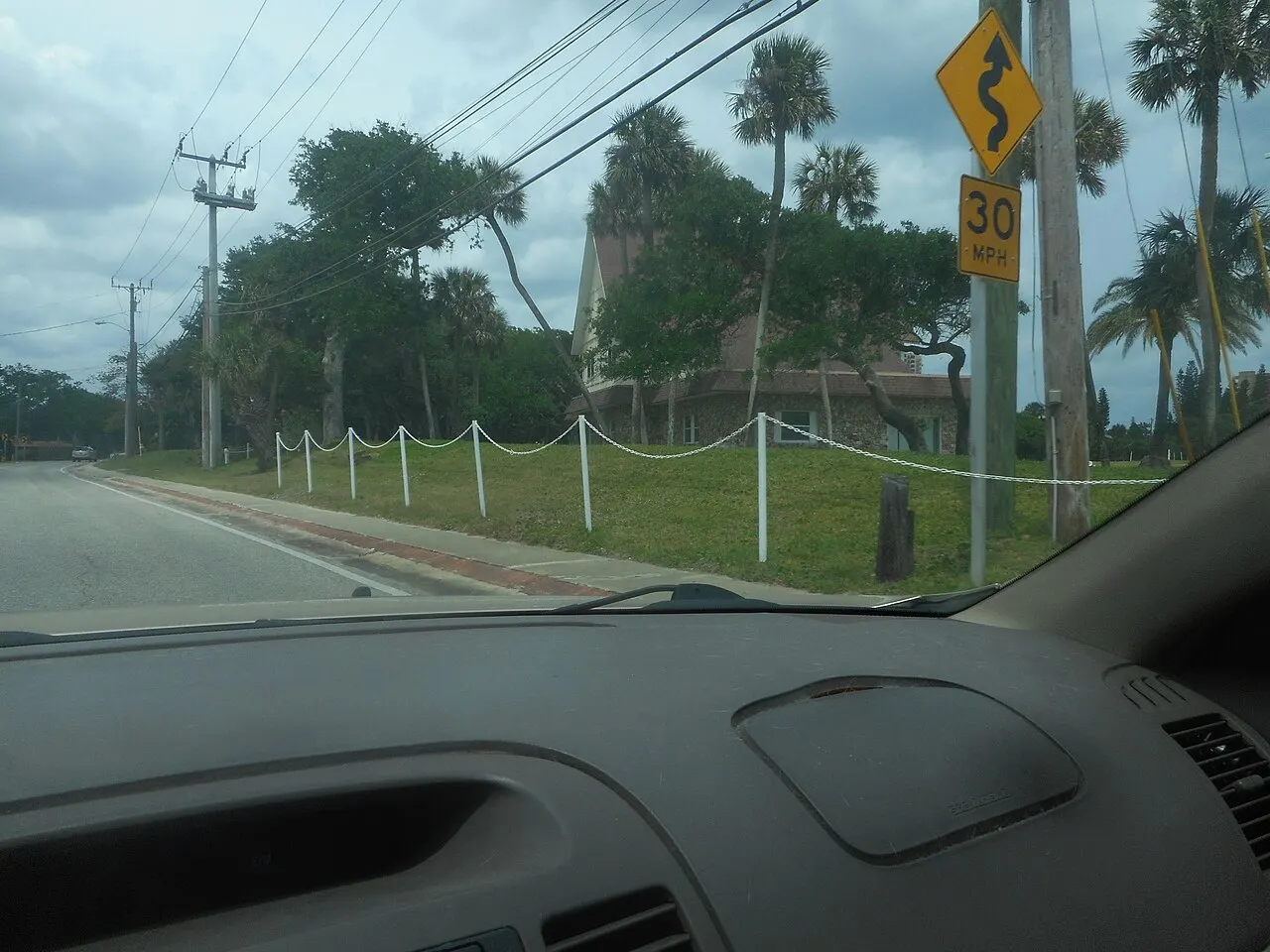 Yellow 30 MPH advisory speed plaque mounted under a Winding Road warning sign, seen through a windshield in Daytona Beach Shores, Florida