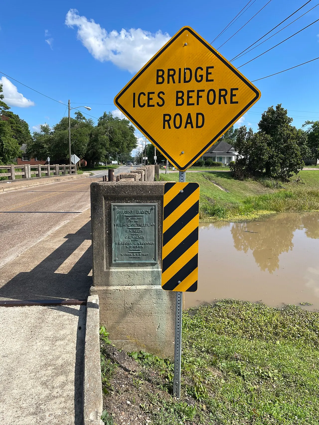 BRIDGE ICES BEFORE ROAD warning sign above a striped object marker at a small bridge in Tallulah, Louisiana