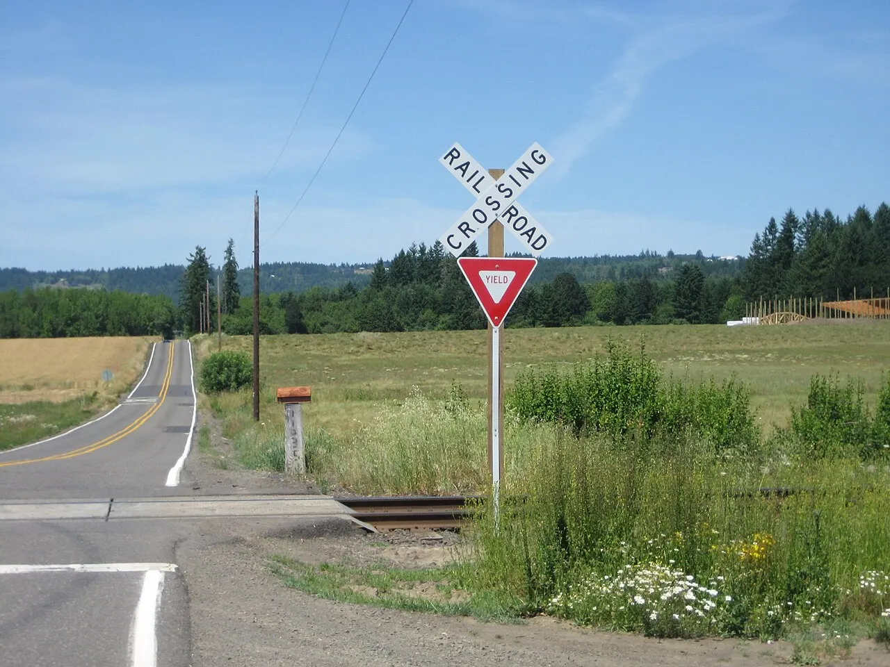 White RAILROAD CROSSING crossbuck with a YIELD sign on the same post at a rural track crossing in Oregon