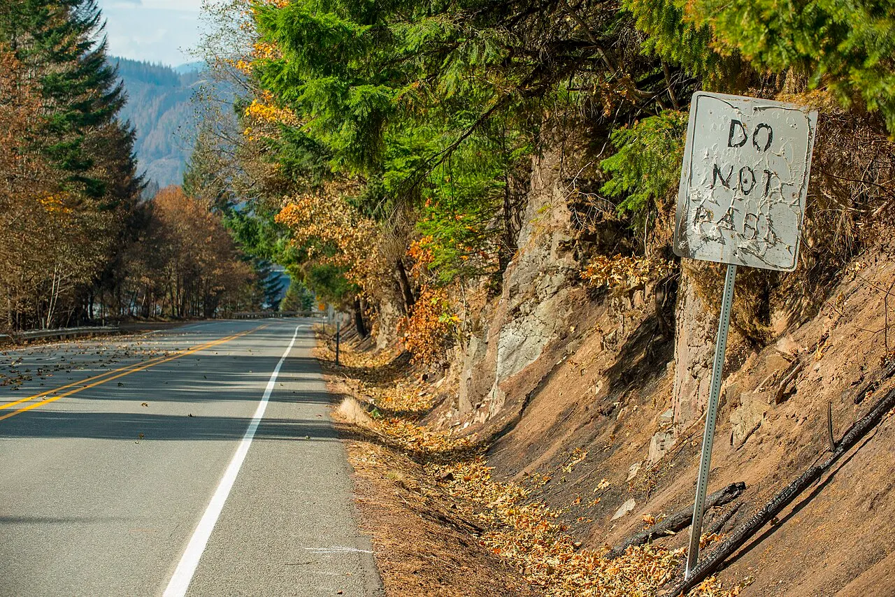 Fire-scorched Do Not Pass sign beside a two-lane highway with a double yellow center line in Oregon