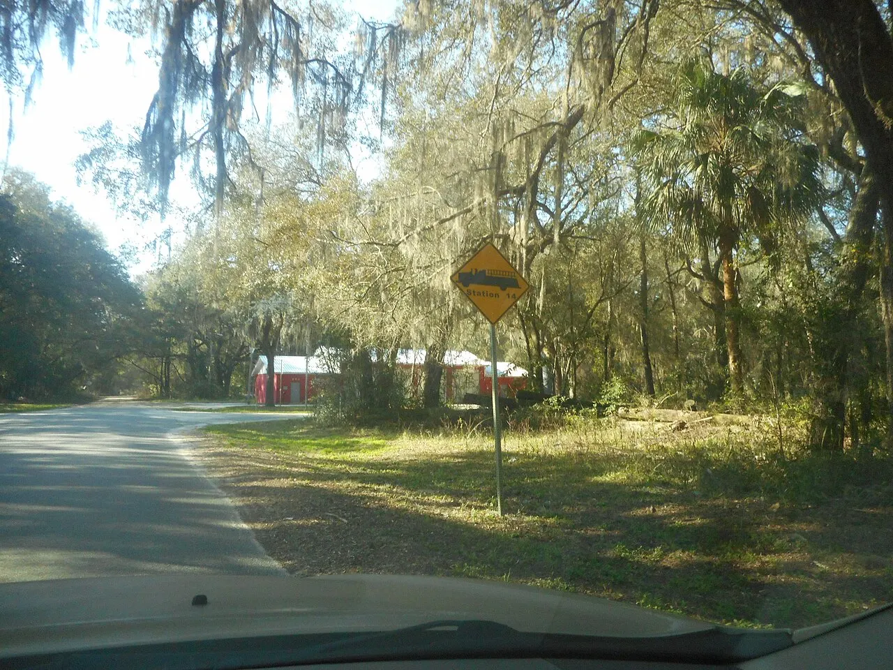 Yellow diamond sign with a fire truck symbol and the words Station 14 beside a wooded road in Florahome, Florida
