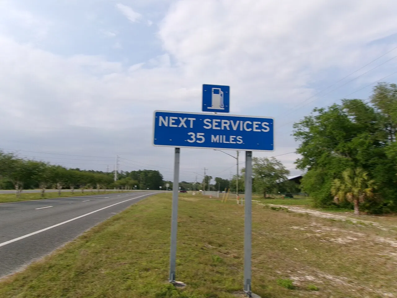 Blue gas pump symbol sign above a NEXT SERVICES 35 MILES panel beside a highway in Inglis, Florida