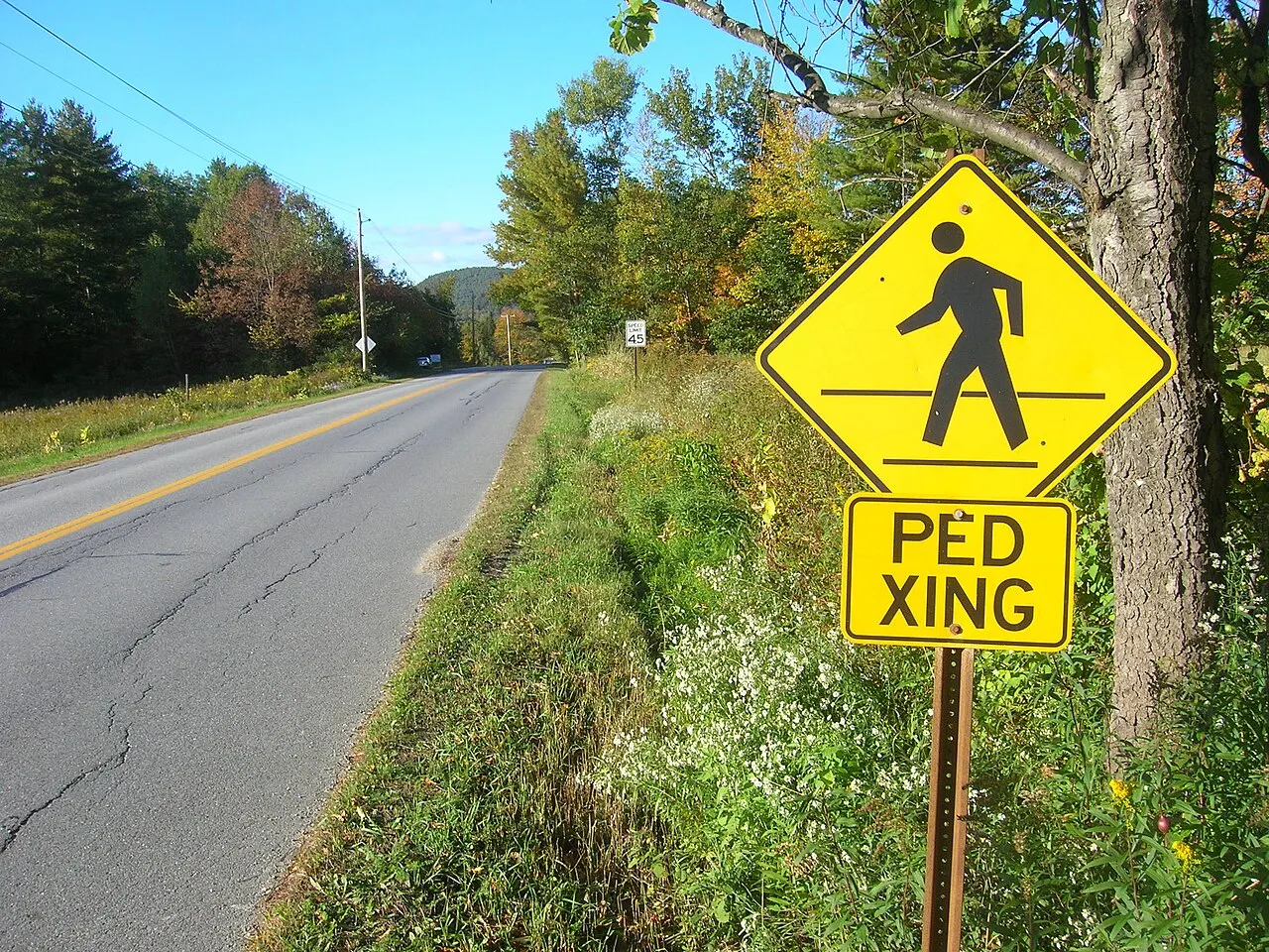 Yellow diamond pedestrian sign with a PED XING plaque beside a rural two-lane road in Huntington, Vermont