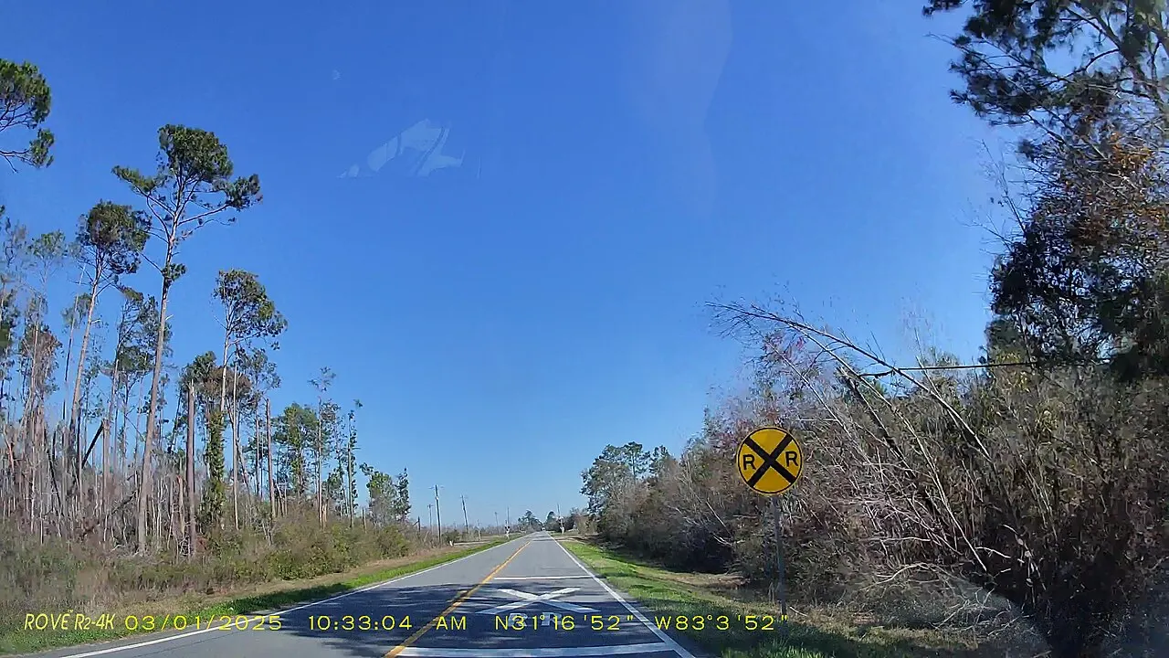 Round yellow railroad crossing advance warning sign beside a rural highway with a white X painted on the pavement