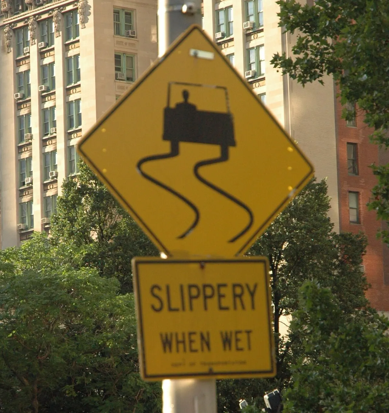 Yellow diamond Slippery When Wet sign showing a car with skid marks, with a SLIPPERY WHEN WET plaque below, on a pole in Manhattan