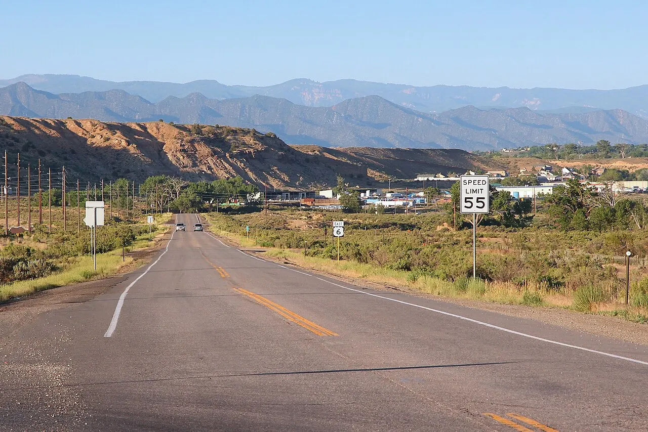 Speed Limit 55 sign on the right shoulder of two-lane U.S. Route 6 with mesas behind