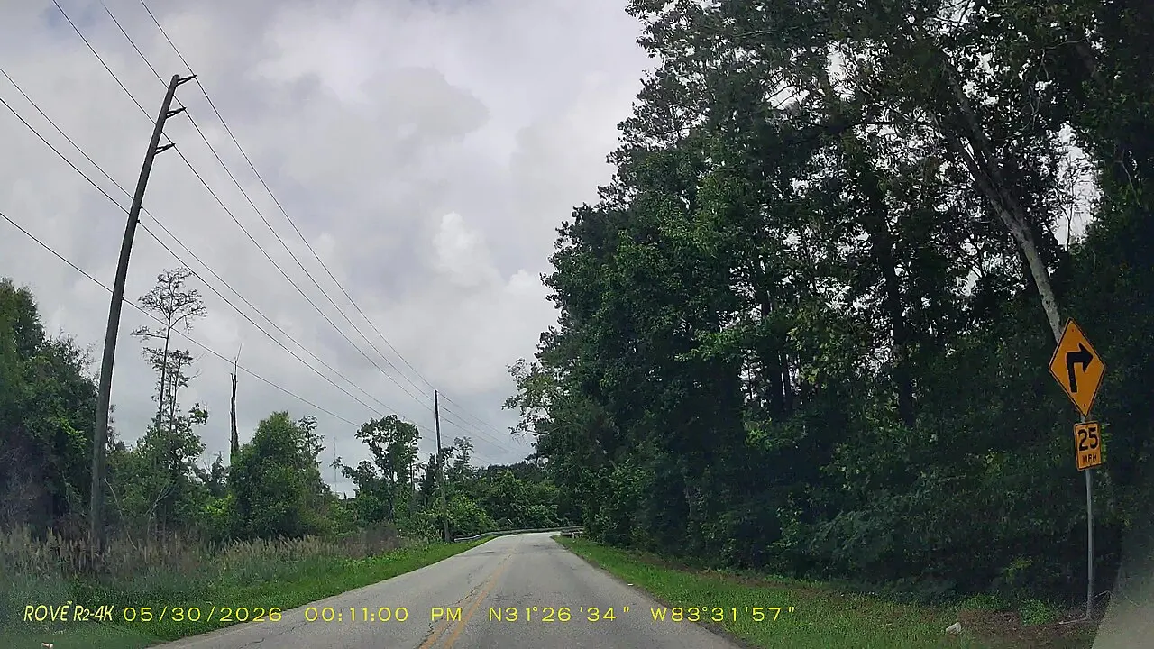 Yellow Turn warning sign with a right-angle arrow and a 25 MPH advisory speed plaque beside a wooded road in Tift County, Georgia