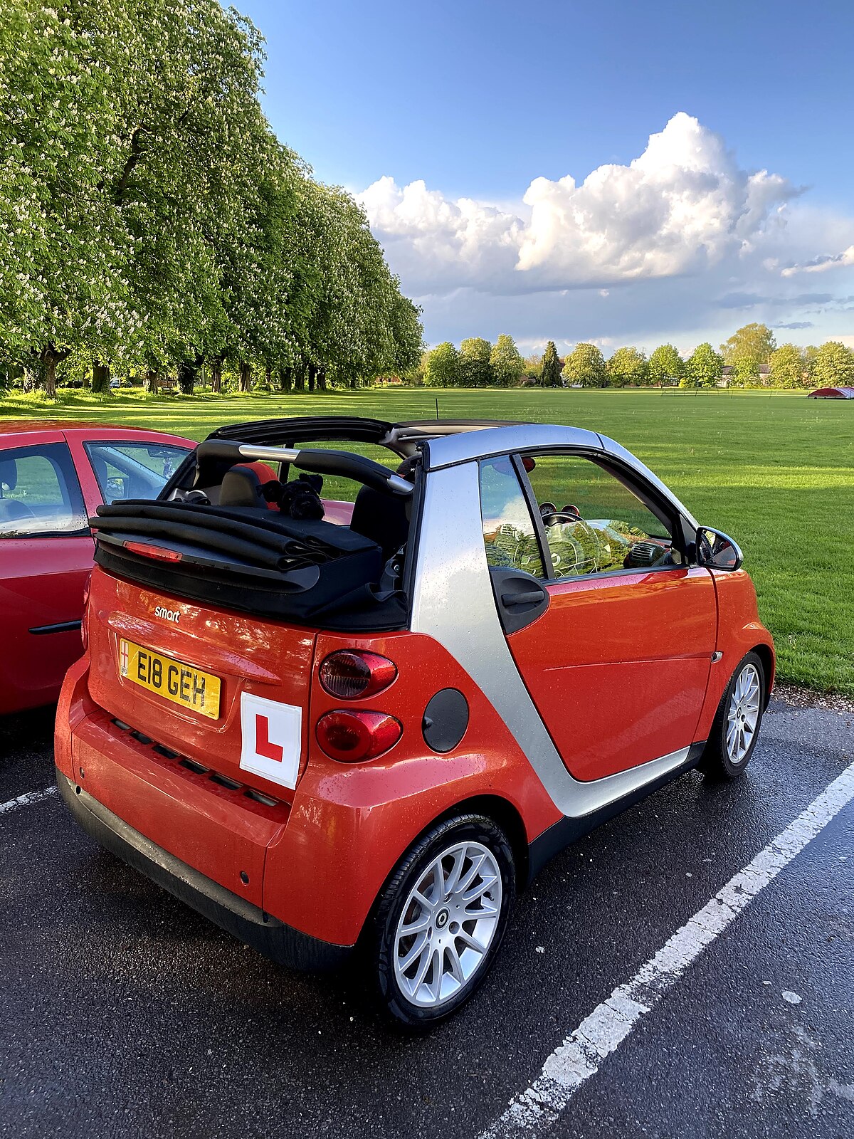 A compact learner car with L-plates parked in a UK residential street, the type of vehicle used for most UK practical driving tests