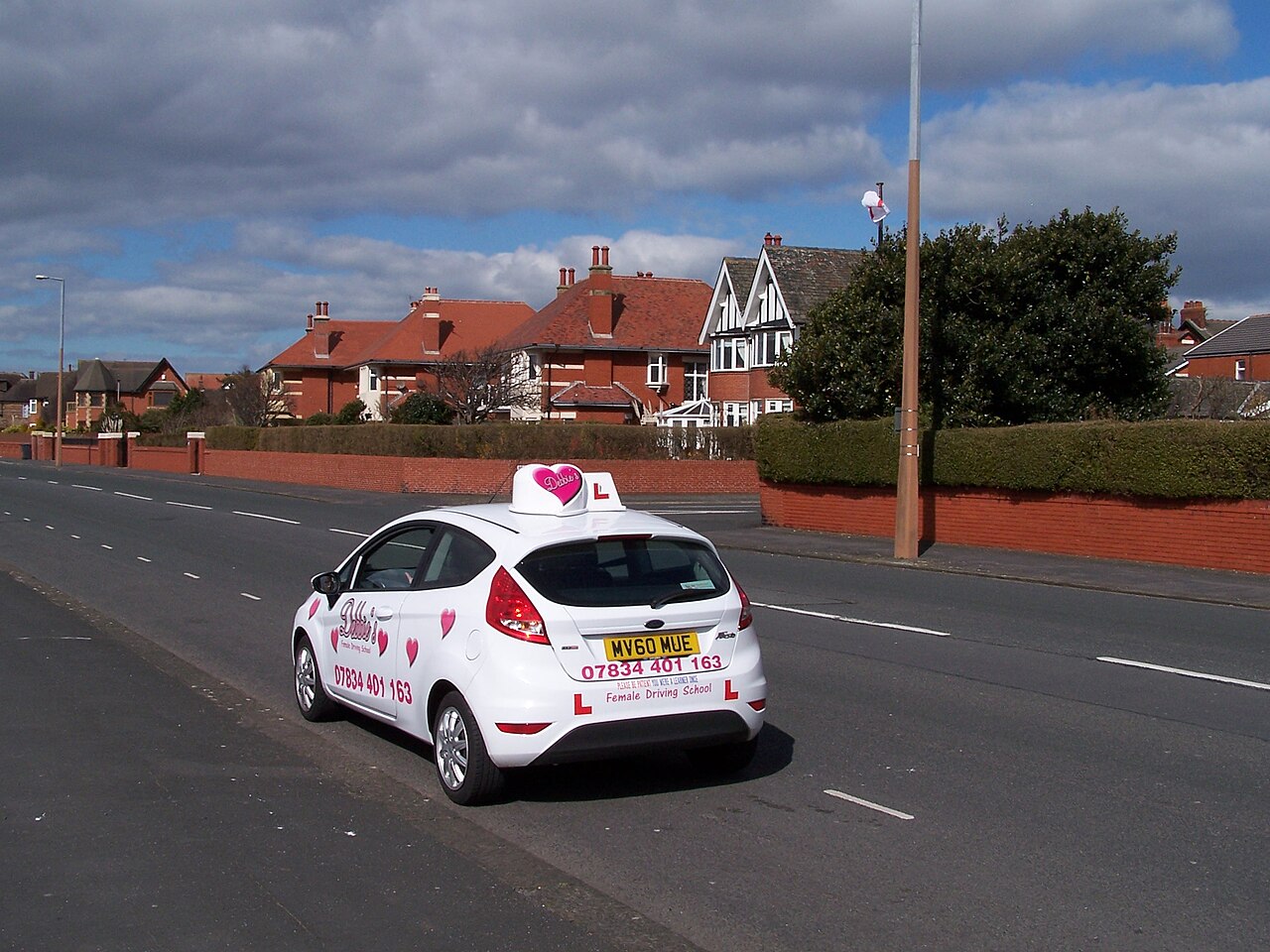 A UK driving-school car with roof sign and L-plates, the lesson context where the age-gap effect first shows up