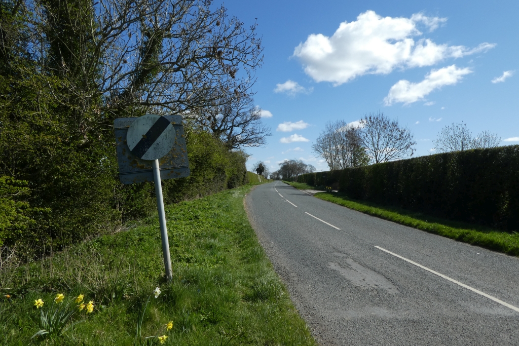 A UK national speed limit sign on a rural road, white circle with diagonal black bar
